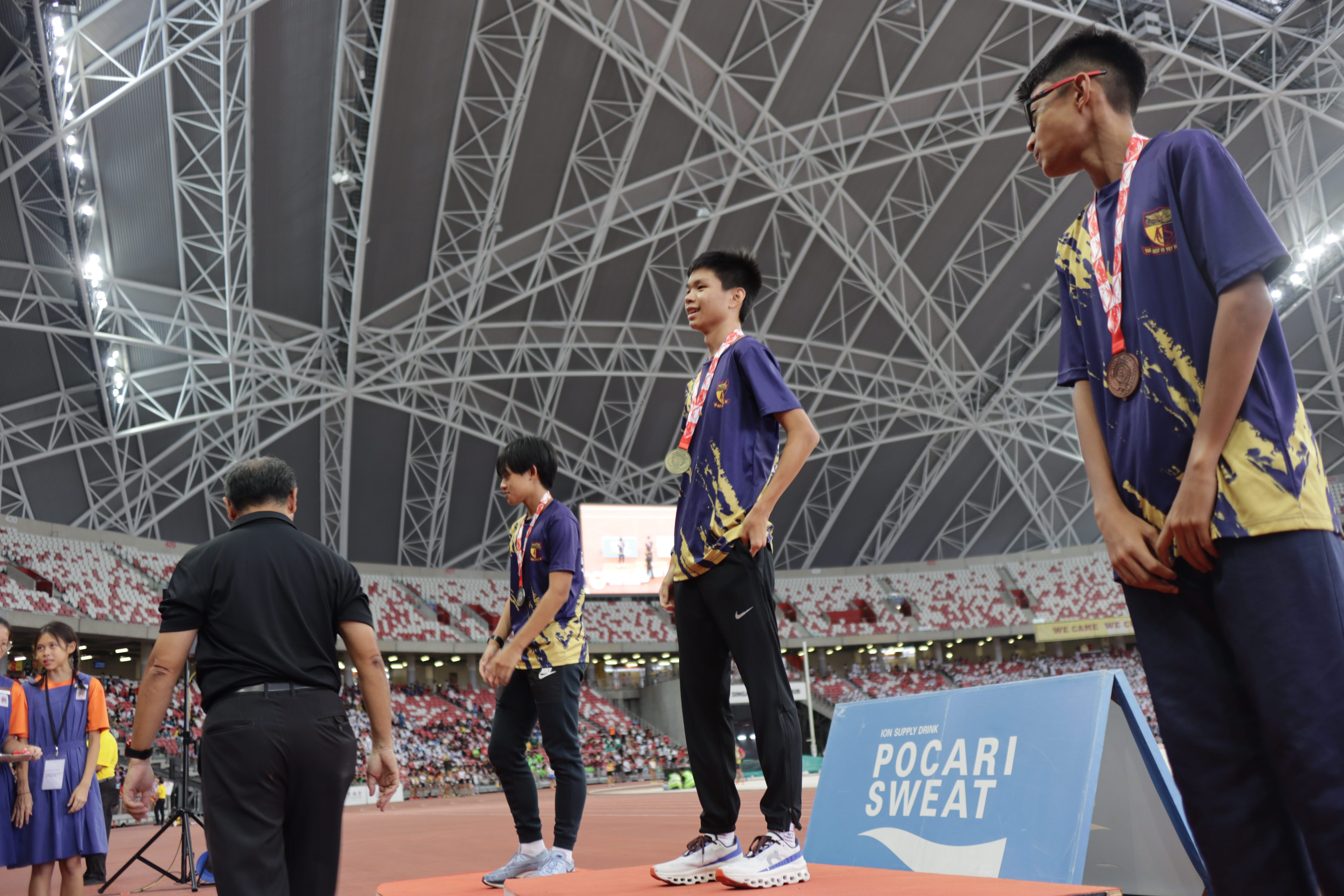 3 students stand on a podium, each wearing a medal